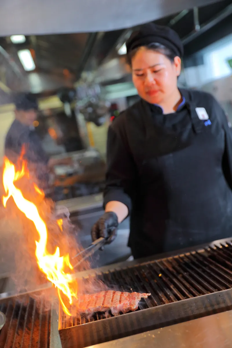 高く上がる炎の前でステーキを焼くシェフ