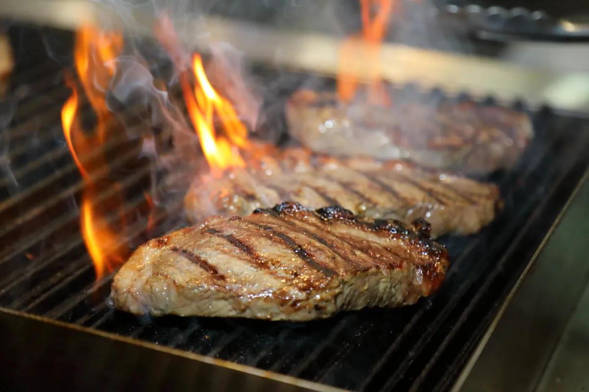 グリルの網の上のビーフステーキ。くっきりとした焼き目、肉のまわりに炎が上がる
